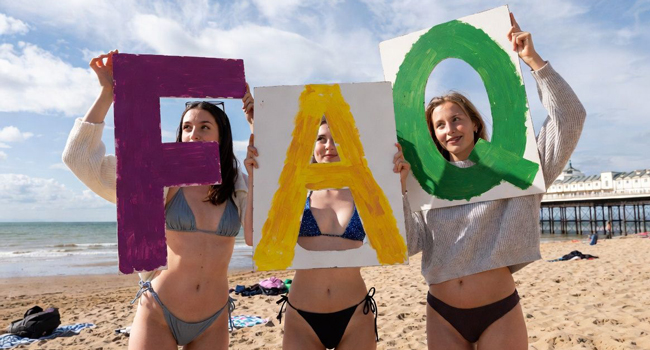 Drei Teilnehmerinnen am Strand in Bournemouth halten FAQ-Schilder während einer LISA! Sprachreise in England
