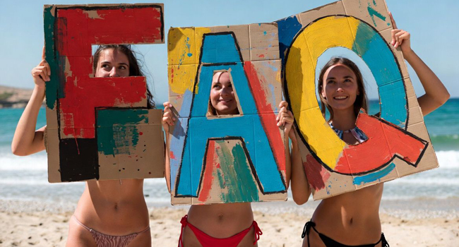 Drei junge Frauen am Strand halten FAQ Schilder während einer LISA! Sprachreise