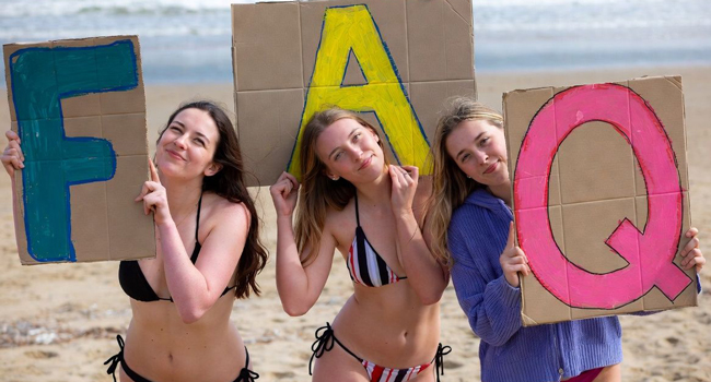 Drei Teilnehmerinnen am Strand in Bournemouth halten FAQ-Schilder während einer LISA! Sprachreise in England