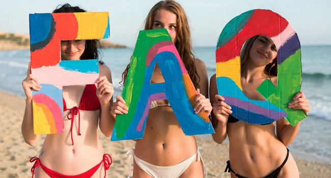 Drei Schülerinnen am Strand halten bunte FAQ-Buchstaben während einer LISA! Sprachreise in Malta