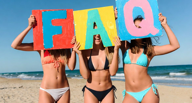 Erwachsene Teilnehmerinnen einer Sprachreise in Malta am Strand mit Schildern für häufige Fragen und Antworten