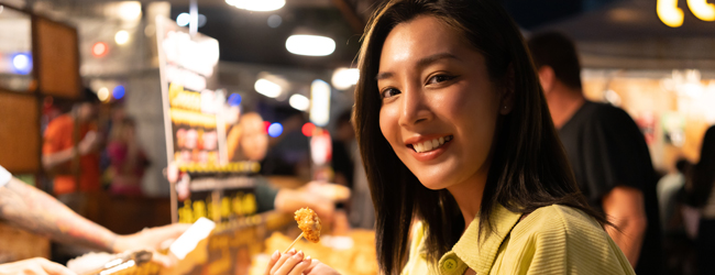 Essen und ausgehen in Bangkok bei einer Sprachreise Eine asiatische Frau probiert etwas an einem Essenstand in Bangkok