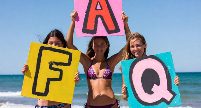 Drei Schülerinnen am Strand in Bournemouth halten FAQ Schilder während einer LISA! Sprachreise