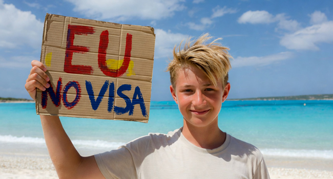 Schüler einer Englisch-Sprachreise in Malta am Strand mit Schild zur visumfreien Einreise für EU-Bürger