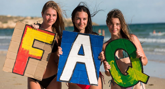 Drei Schülerinnen am Strand in Malta halten große FAQ-Buchstaben während einer LISA! Schülersprachreise