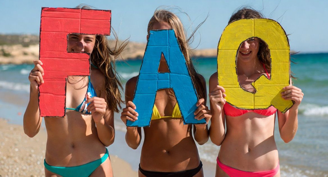 Drei Schülerinnen einer Schüler-Sprachreise in Malta am Strand von St. Julian’s mit großen FAQ-Buchstaben
