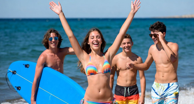 Mädchen reckt Arme nach oben im Hintergrund drei Jungs mit Meer