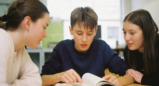 Drei Kinder lesen gemeinsam in einem Schulbuch