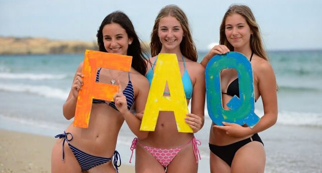 Young Adults am Strand in Mallorca halten FAQ Buchstaben während einer LISA! Sprachreise mit Meer im Hintergrund
