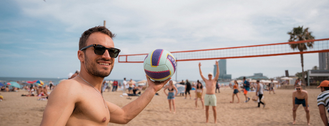 Ein junger Mann mit Sonnenbrille wirft einen Volleyball am Strand von Barcelona