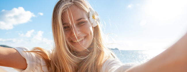 Eine blonde Frau mit Blume im Haar vor dem blauen Meer