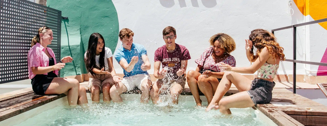 Sprachschüler sitzen am Pool der Sprachschule in Sevilla und plantschen mit den Beinen im Wasser