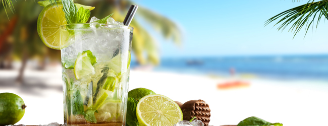 Ein Glas Mojito mit Zitrone und Eis am Strand mit Meer im Hintergrund
