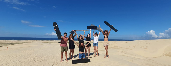 Cooler Ausflug an den Strand in Sydney Mehrere Menschen posieren mit erhobenen Händen und Skateboards am Strand vor dem Meer in Sydney