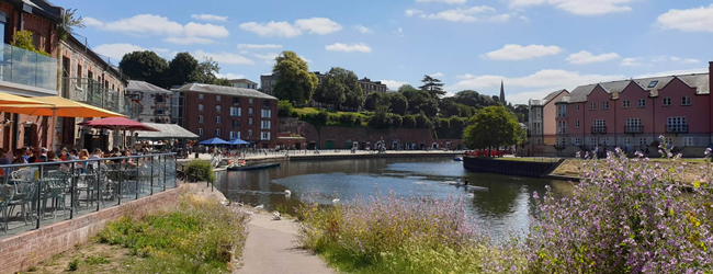 Blick auf den Fluss in Exeter mit Blumen und voll besetzten Cafés am Ufer