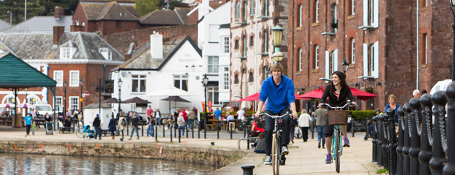 Zwei personen fahren Fahhrad am Ufer des Flusses in Exeter im Hintergrund Menschen und Cafes
