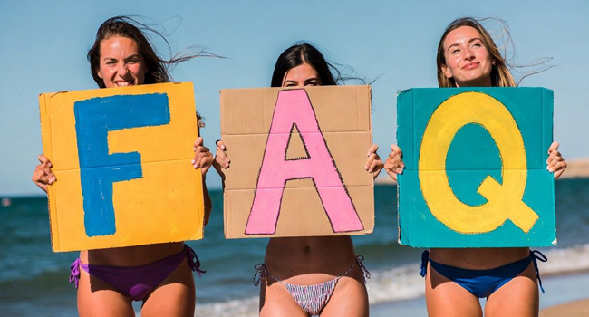 3 Frauen mit Pappschildern am Strand Malta mit Aufschrift FAQ