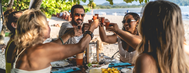 Mehrere Erwachsene sitzen am Strand und essen und trinken gemeinsam