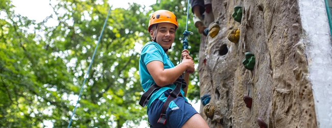 Abseilen an einer Kletterwand als eine Aktivität bei Adventure England Ein Schüler mit gelbem Helm selt sich gerade eine Kletterwand ab bei einer Schülersprachreise