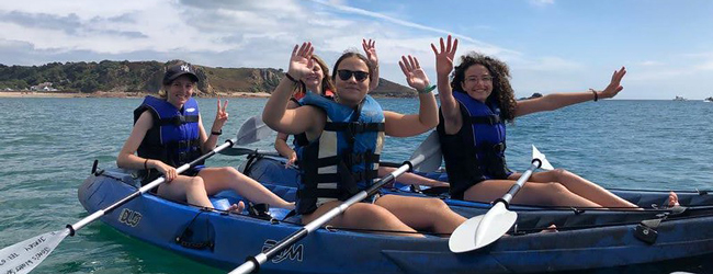 Vier Mädchen winken in die Kamera und sitzen in Paddelbooten bei einer Sprachreise in Jersey