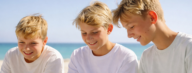 Drei blonde Jungen sitzen am Meer