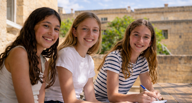 Drei Mädchen sitzen draussen in Malta Sliema und lernen gemeinsam und lachen in die Kamera