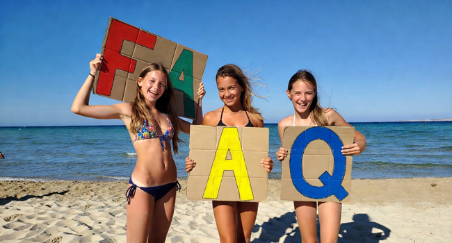 Drei Mädchen am Strand in Malta halten Buchstaben F A Q in die Höhe.