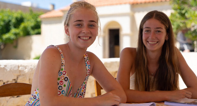 Zwei Mädchen lächeln in die Kamera und lernen gemeinsam bei einer Schülersprachreise