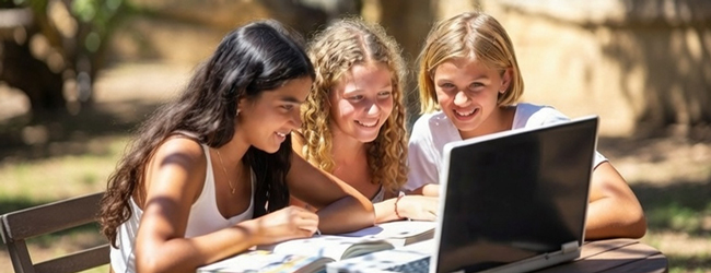 Drei Mädchen sitzen in einem Garten und schauen gemeinsam in einen Computer